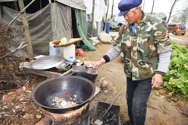 西岸,一位村民在一个废旧油桶掏空做成的露天大锅灶上生火做大锅鱼