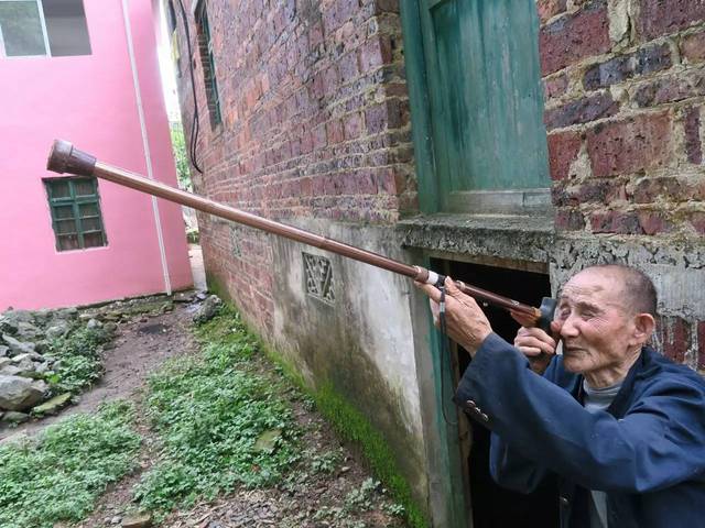 101岁的蒋义青老人,拿着自己的拐杖当步枪,做了一个瞄准的姿势.