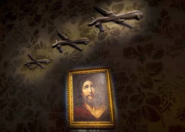 这是一块装饰着军用无人机浮雕和耶稣画像的墙壁,耶稣前额上一颗狙击
