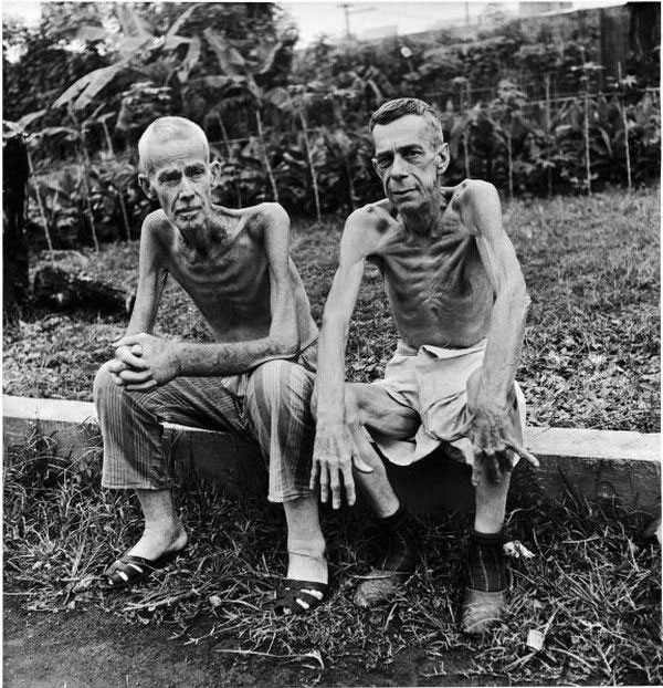 1945 菲律宾 马尼拉 两个骨瘦如柴的美国人坐在日军的集中营外面,他们
