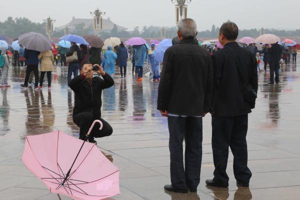 两位老人在广场上合照,雨伞随手倒放在一旁