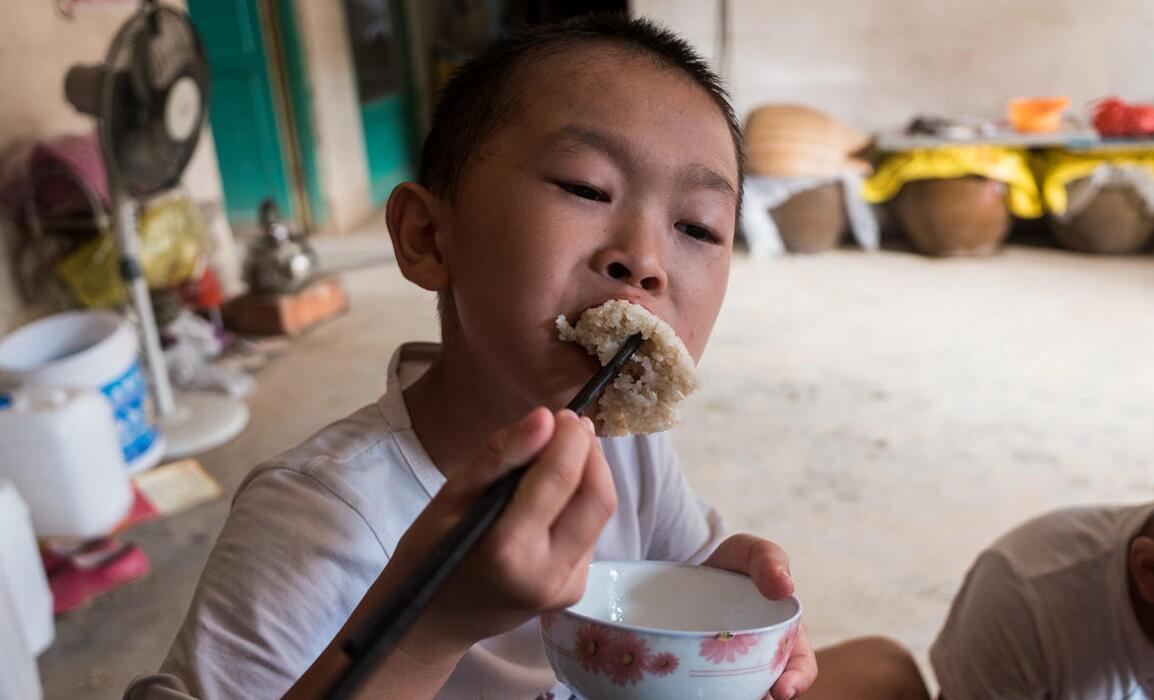 一个孩子正在吃老人做好的糯米饭,直接吃了一碗,还吵着要吃婆婆做的