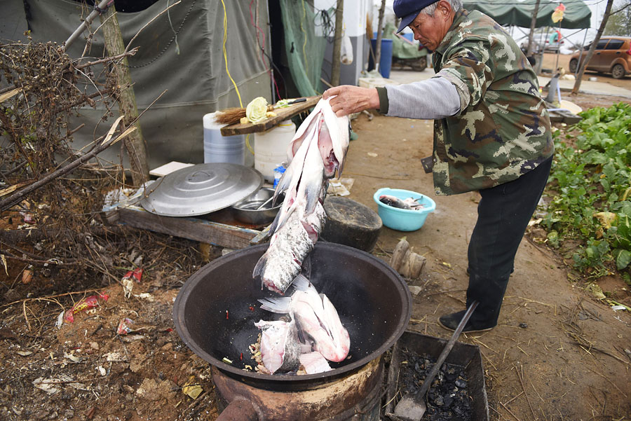 西岸,一位村民在一个废旧油桶掏空做成的露天大锅灶上生火做大锅鱼