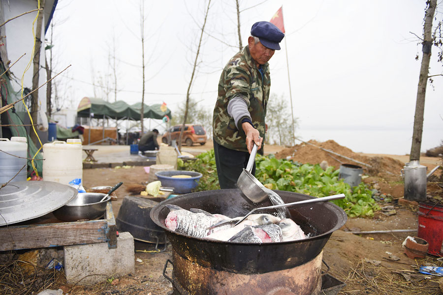 一位村民在一个废旧油桶掏空做成的露天大锅灶上生火做大锅鱼