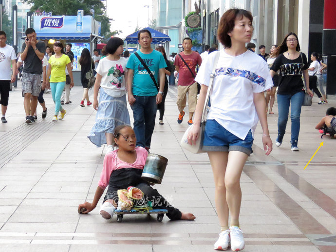 2,王府井大街上,一位双腿残疾的女青年坐在滑轮车上沿街乞讨.