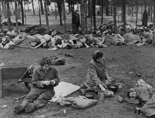 一群德国女人在用餐,边聊边吃,不远处是一堆犹太人的尸体