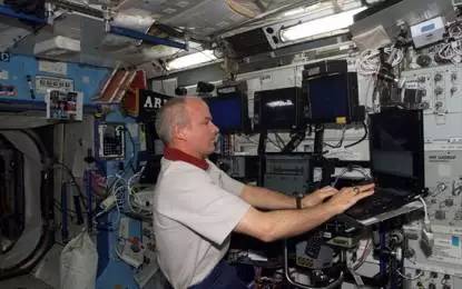 身穿舱内工作服的宇航员在使用个人电脑进行工作