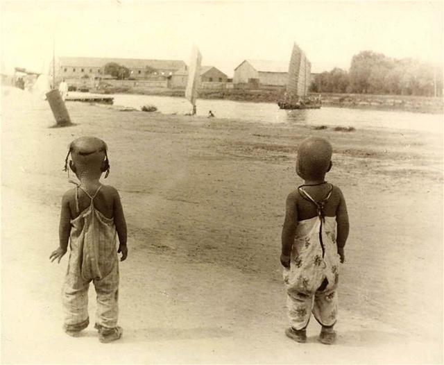两个穿着开裆裤的孩子望着河道里的船只
