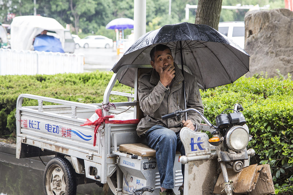 在雨中等活的农民,打着伞,吸着烟,也不舍得找地方避雨.