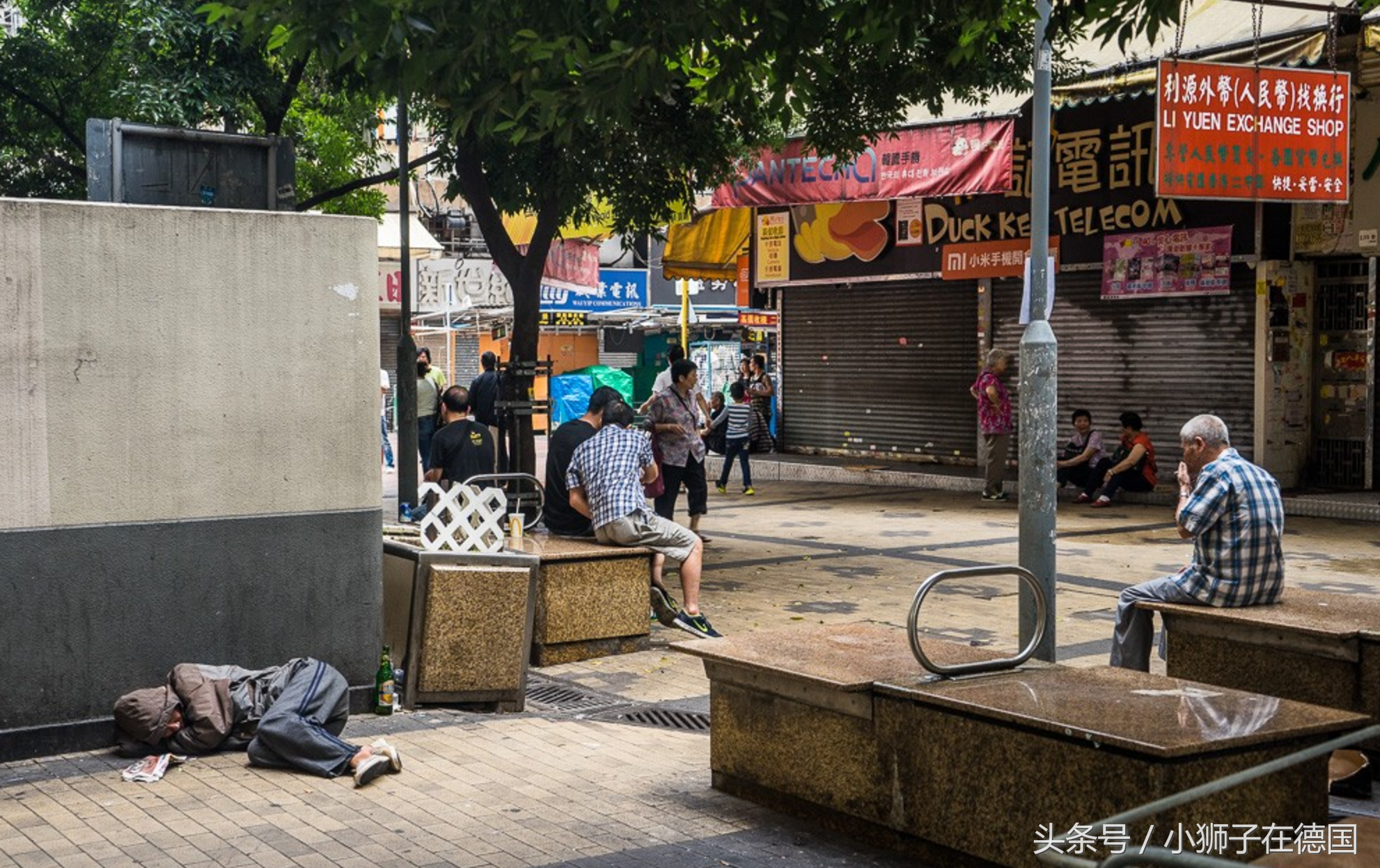 街道拐角处,一名长者坐在石凳上吸烟;离他不远处,一名流浪汉卷缩在墙