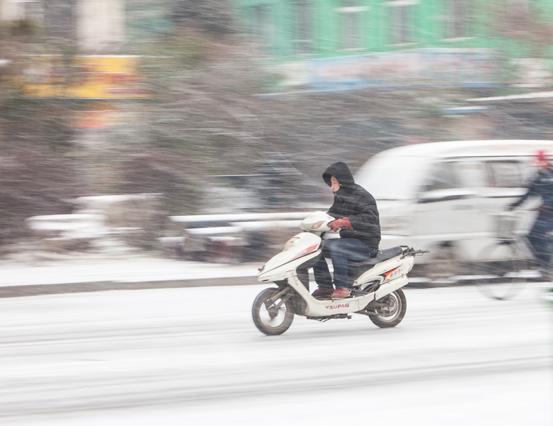 清理隔离护栏的清洁工视线不好,汽车亮起了大灯一家三口雪中骑行银装