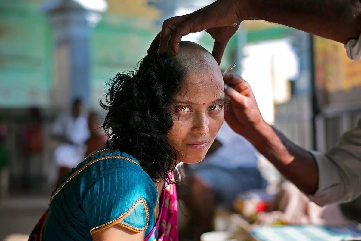 一名印度女子在寺庙里被剃光头发,她相信把头发捐赠给神灵可以治好